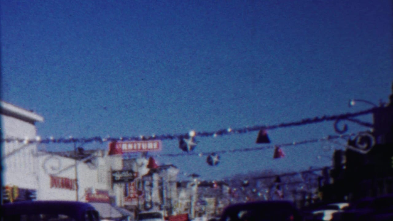 Festive street decorations stretch above storefronts and parked cars under a clear sky.