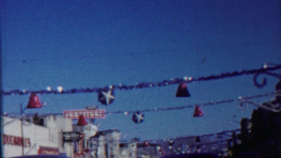 Decorated Saint Francis commercial street in 1959, with red bell ornaments, stars, storefront signs, and vintage cars.