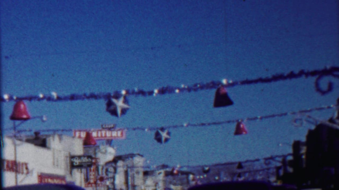 Decorated street with hanging bells, star ornaments, storefronts, and a blue sky.