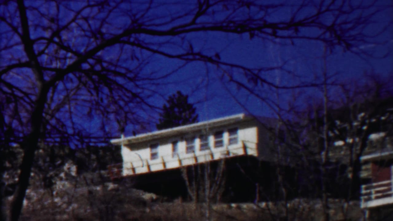 White house on a hillside framed by bare tree branches and a blue sky.