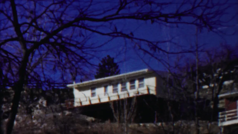 White hillside house in Saint Francis, Kansas, seen through bare branches in soft, blue-shifted 1959 8mm footage.