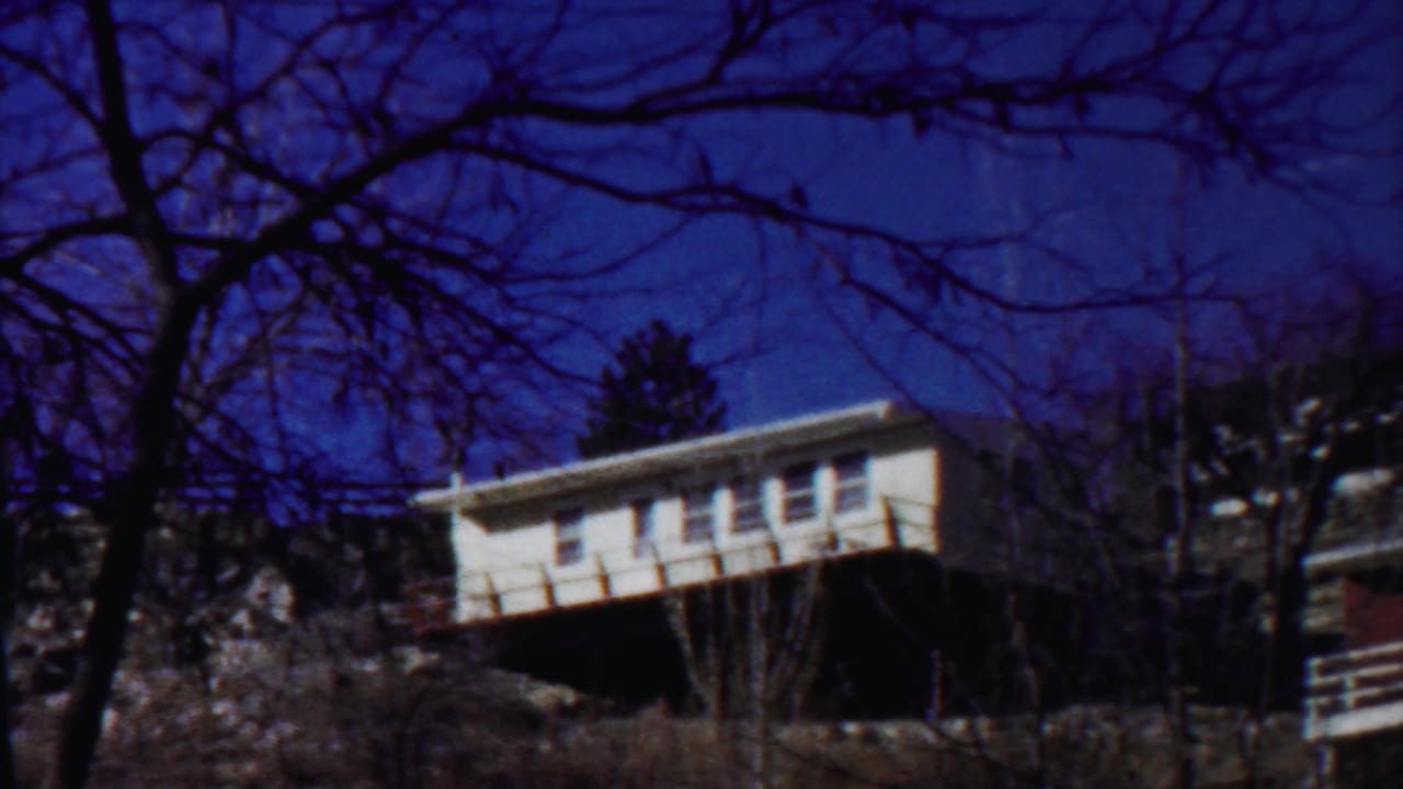 1959 Saint Francis, Kansas 8mm frame showing a white modern house raised above a rocky slope under a deep blue sky.