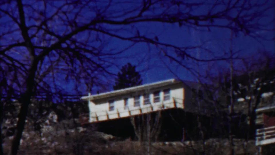 1959 Saint Francis, Kansas 8mm frame showing a white modern house raised above a rocky slope under a deep blue sky.