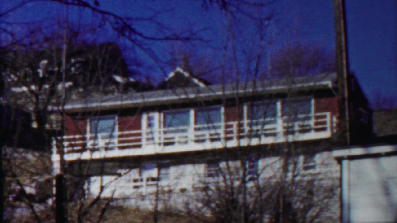 Two-story building with white balcony railings, red panels, bare trees, and blue sky.