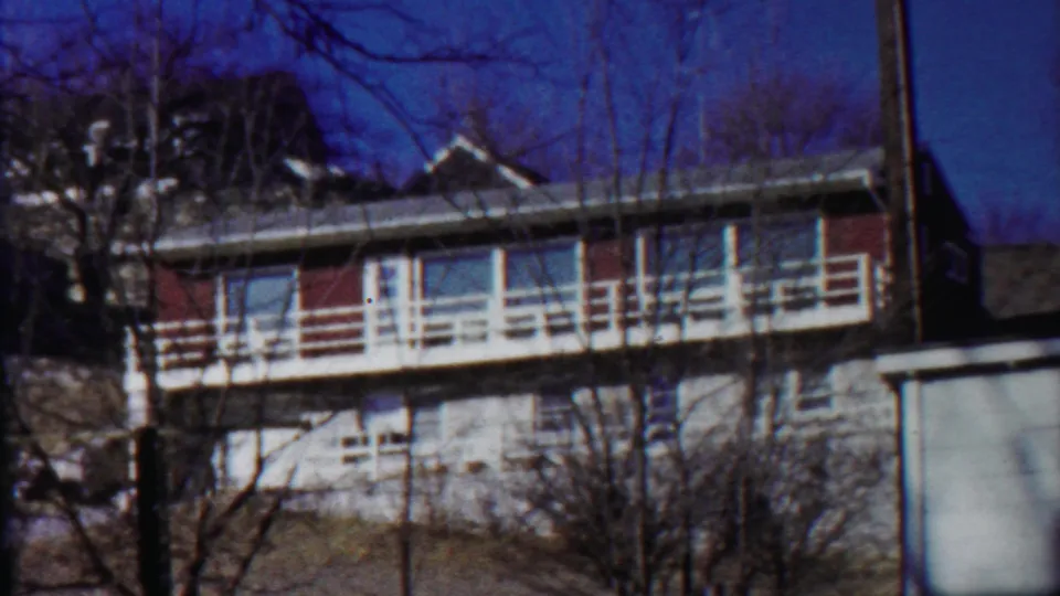 Soft 1959 home-movie frame of the Saint Francis apartment building, with white railings and winter branches in front.