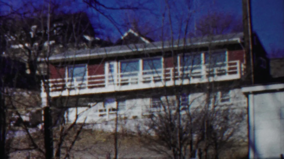 Saint Francis, Kansas 8mm frame showing the apartment building facade, white balcony rail, bare trees, and adjacent pale wall.