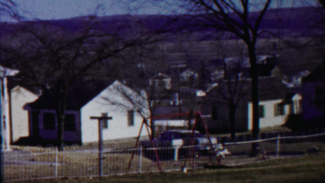 White houses, a yard fence, bare trees, a swing set, and a parked car.