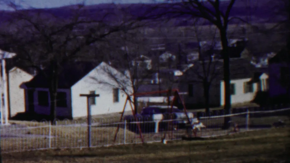 Saint Francis, Kansas residential scene showing small white houses, a fenced yard, bare trees, and a red swing set in 1959 footage.