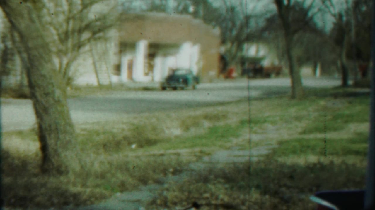 Wide 1959 Saint Francis, Kansas street view with grass in the foreground, bare trees, and small-town buildings beyond the road.