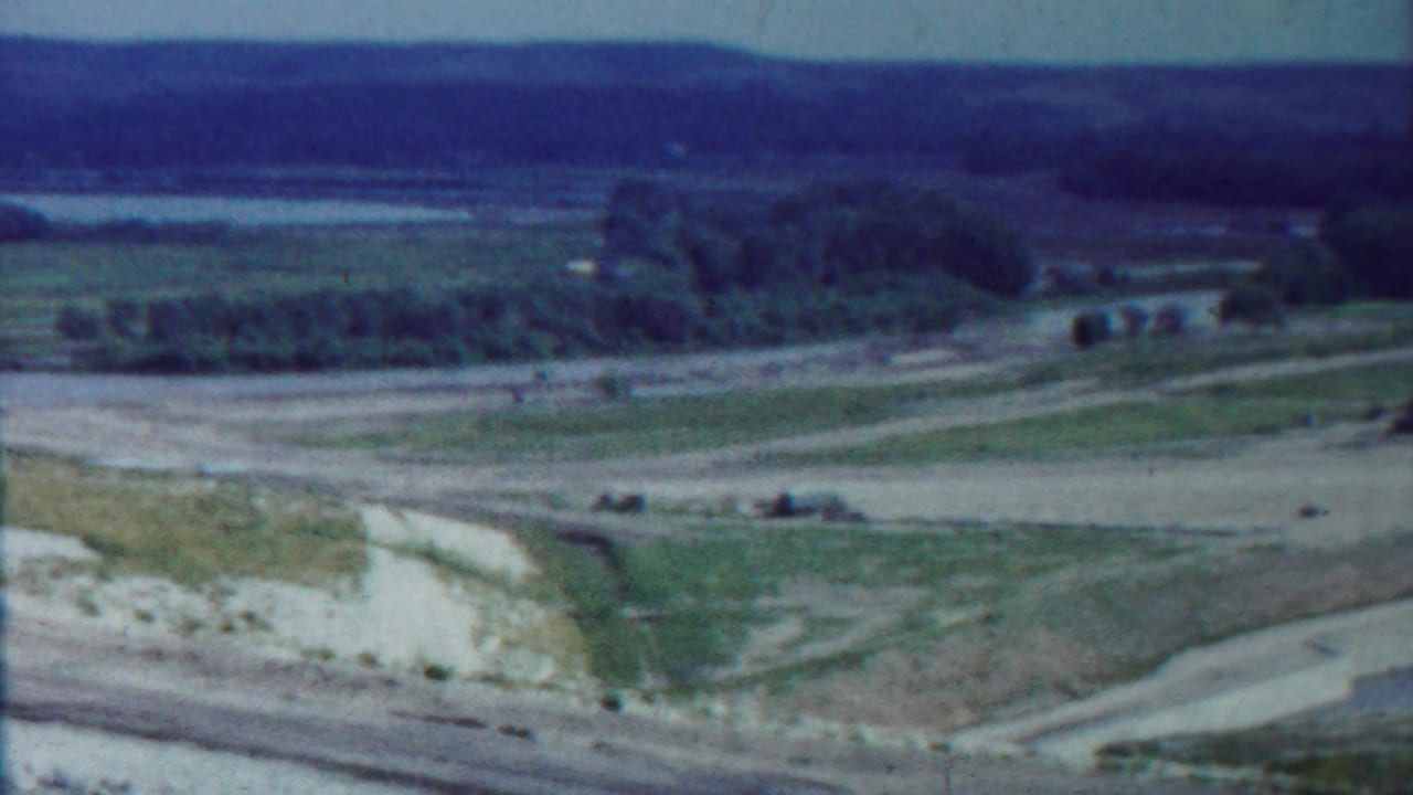 Open countryside with intersecting dirt roads, fields, trees, and a distant waterline.