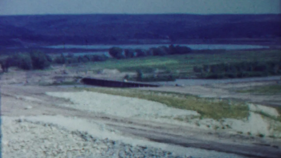 1959 Saint Francis, Kansas frame showing an eroded foreground slope, a low structure, dirt roads, fields, trees, and distant water.