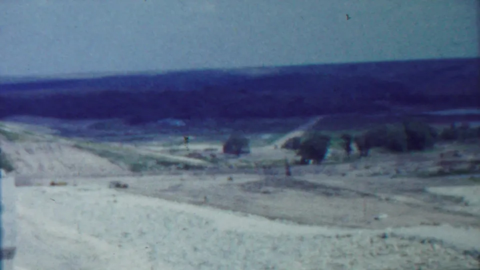 1959 Kansas home-movie view across pale open ground and a dirt road toward sparse trees, low hills, and a distant horizon.