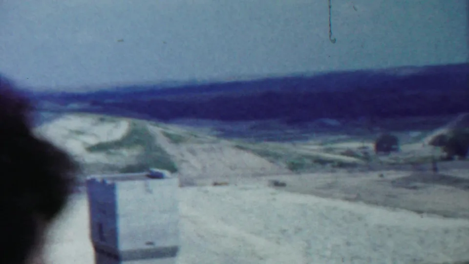 Final Saint Francis, Kansas frame showing a dirt road, open landscape, low hills, sparse trees, and a small structure in the foreground.