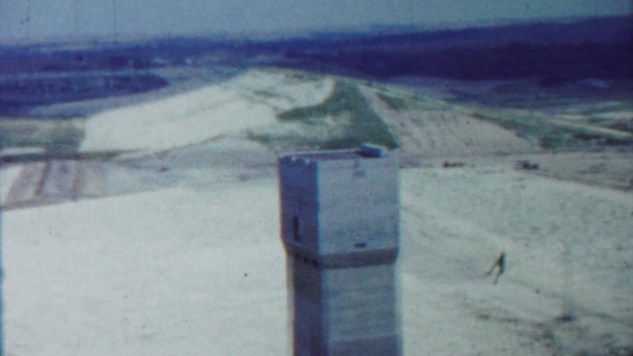 Concrete tower in a pale open landscape with fields and distant horizon.