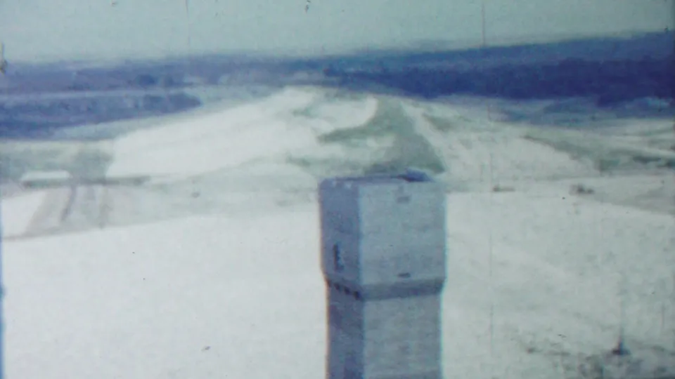 Saint Francis, Kansas home-movie frame with a concrete tower below a hazy horizon and graded pale ground.