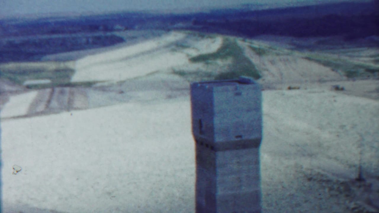 1959 Saint Francis, Kansas 8mm frame showing a concrete tower in front of rolling white and green terrain under a pale blue sky.