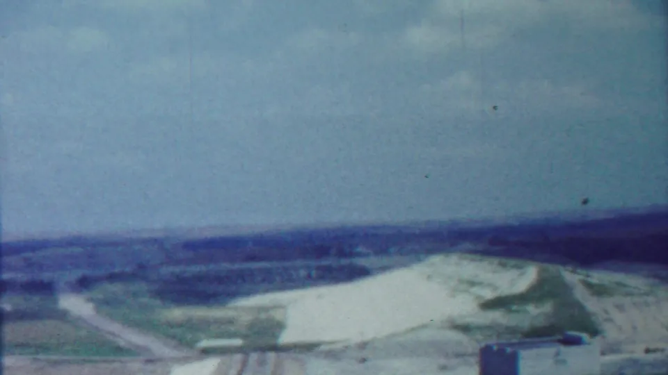1959 Saint Francis, Kansas frame showing a broad white-and-green landscape, distant horizon, and the edge of a tower in the lower right.