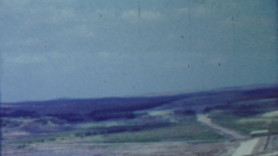 Soft 1959 8mm panorama near Tuttle Creek Dam, with rural fields, a curving road, distant ridgeline, and bright sky.