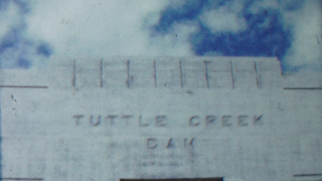 1959 Kansas frame of the Tuttle Creek Dam concrete facade, with engraved lettering, pale sky, and structural seams visible.