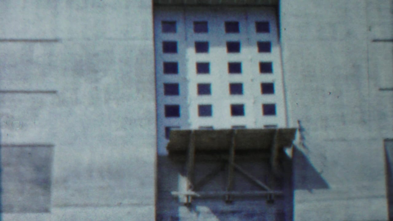Concrete building wall with square window grid and scaffold below.