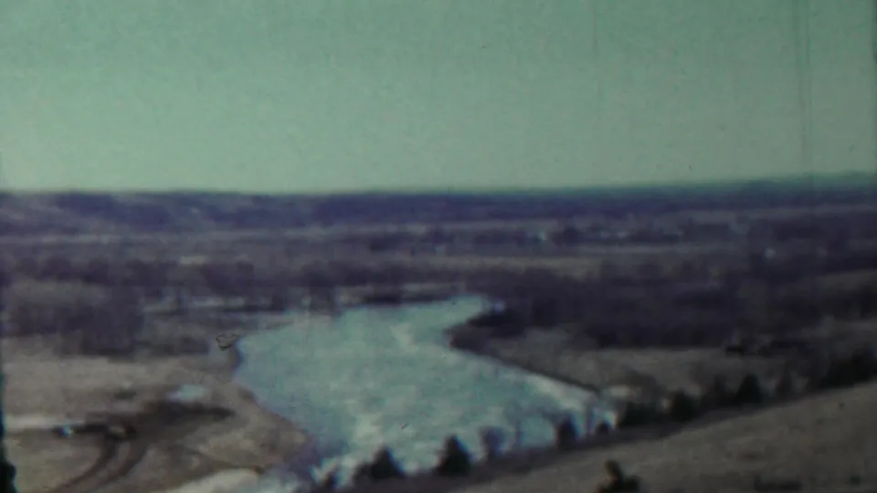 Elevated view of a river bend in the Saint Francis, Kansas area, with fields, tree lines, and faded home-movie color.