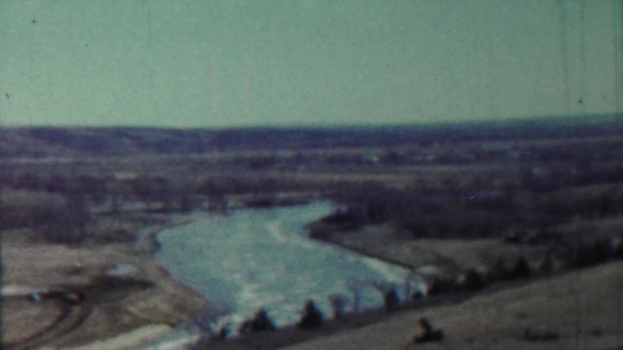 Soft 8mm view of a winding river through open rural land beneath a pale sky.