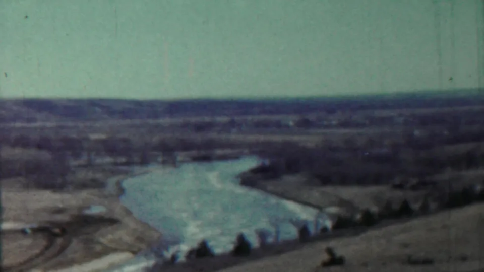 1959 Saint Francis, Kansas home-movie frame showing a winding river, open fields, sparse trees, and distant low hills.