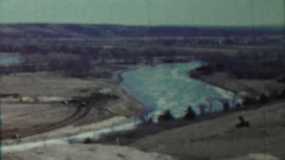 1959 Saint Francis, Kansas home-movie still showing a river valley with open ground, sparse trees, and distant low terrain.