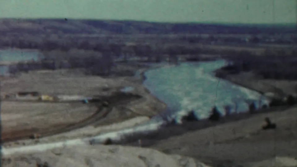 1959 Saint Francis, Kansas frame capturing a winding river beside open fields and sparse trees under a pale sky.