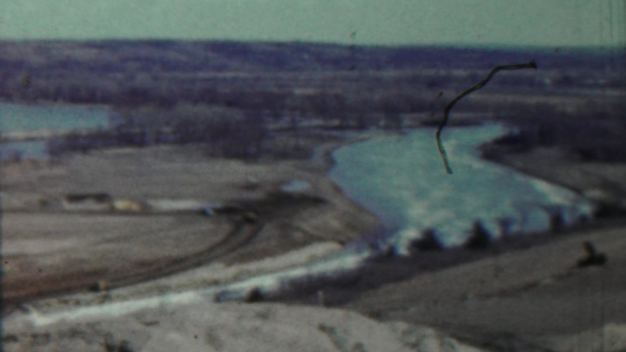Distant lake curve bordered by pale shoreline and open fields under a bright sky.
