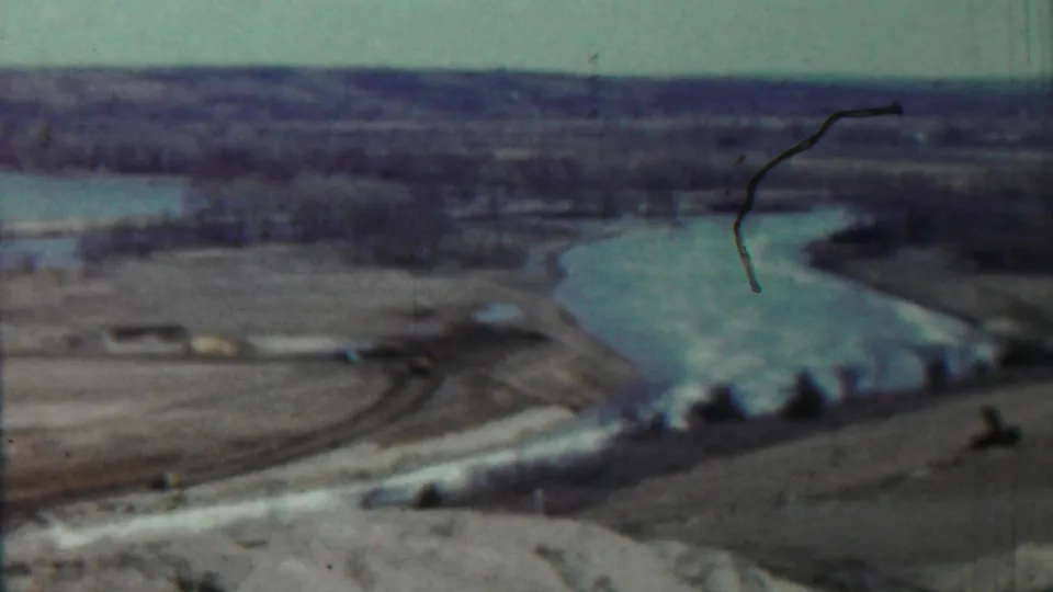 1959 Saint Francis, Kansas 8mm frame showing a soft distant view of a winding lake, pale banks, fields, and sparse trees.