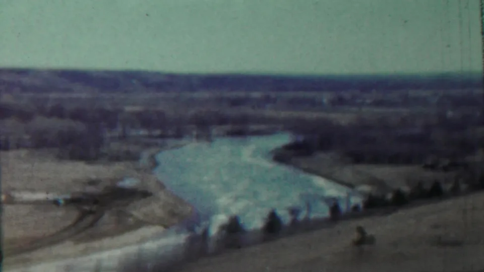 1959 Saint Francis, Kansas frame showing the winding lake, open shoreline, distant tree line, and a small column-like object near the lower right.