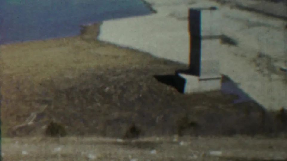 The pan holds on the column and concrete base, with a muted water surface and dry Saint Francis landscape behind it.