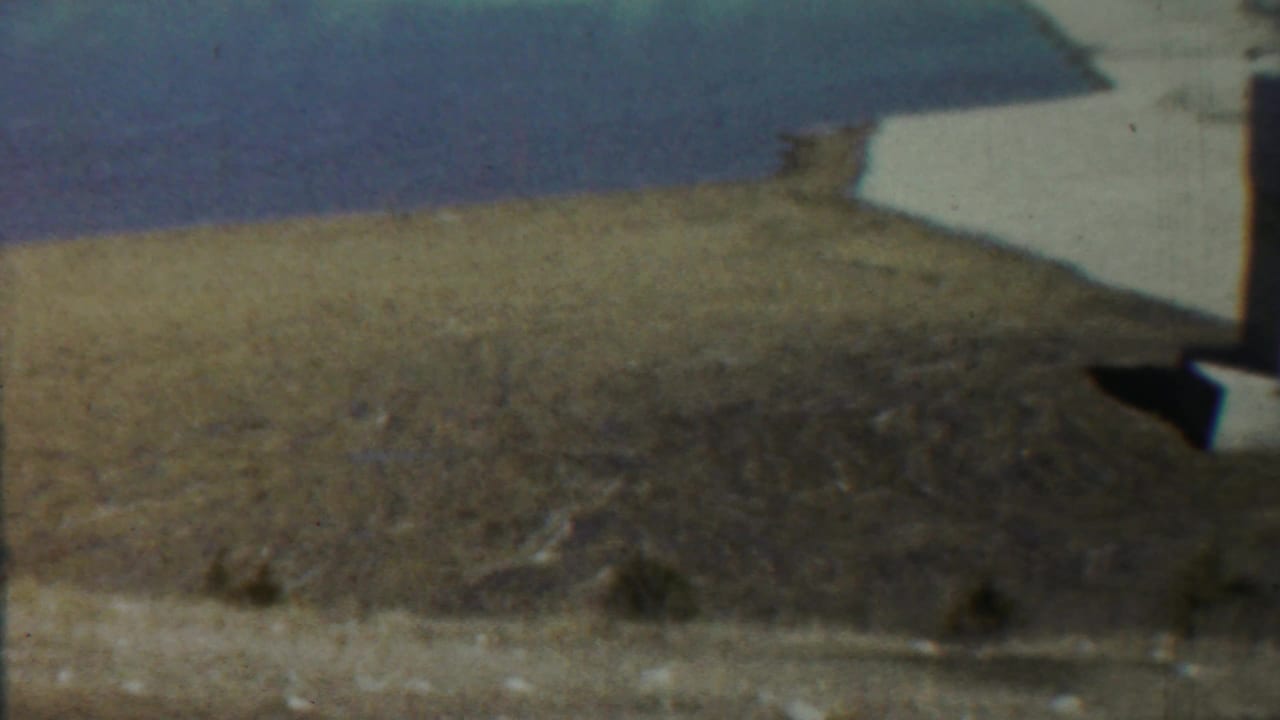 Dry open field under blue sky with a partial white structure at the right edge.