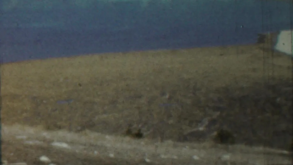 1959 Saint Francis, Kansas 8mm frame with dry grass, low scrub, pale roadside-like ground, and a clear blue sky.