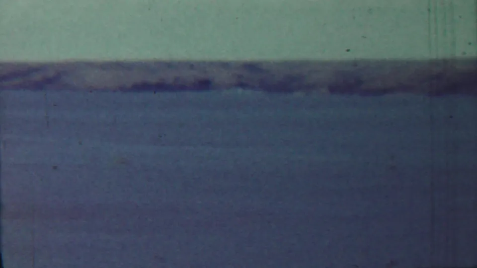 1959 8mm home-movie frame showing open water and a hazy distant shoreline, with no people or structures visible.