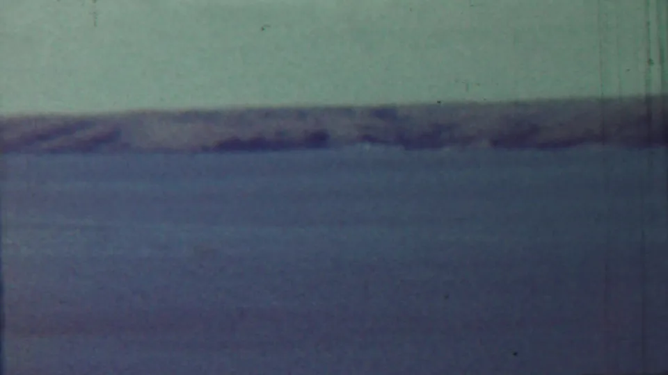 1959 8mm frame from the Saint Francis, Kansas clip showing a quiet body of water and distant low shore in faded color.