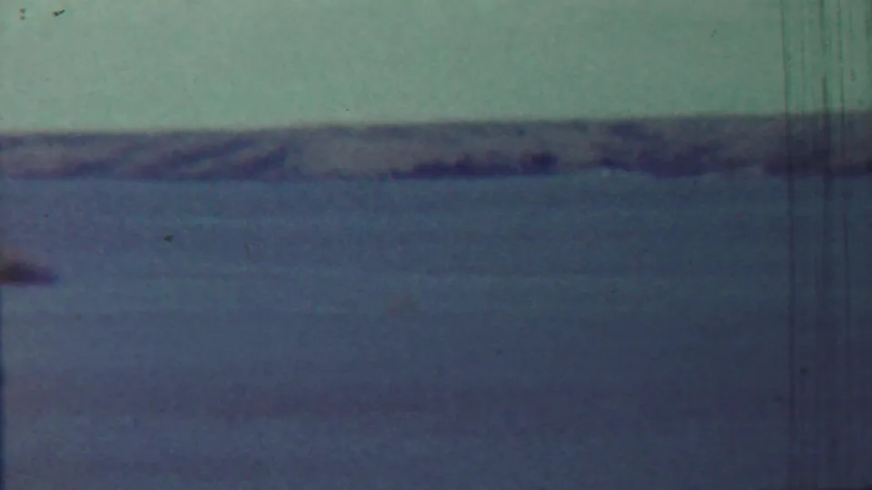 1959 Saint Francis, Kansas frame with calm water, low shoreline, and a small unclear object near the horizon.