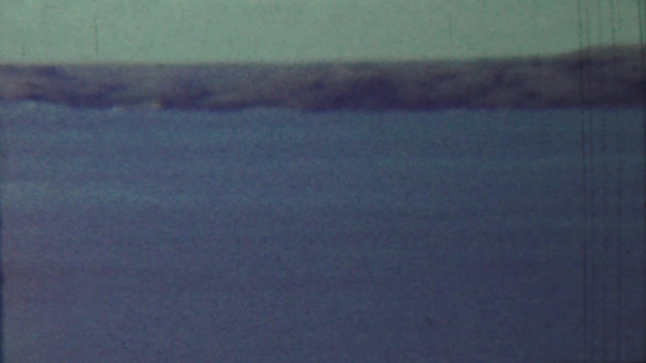 1959 Saint Francis, Kansas 8mm frame showing broad water, muted sky, and a soft dark shoreline across the horizon.