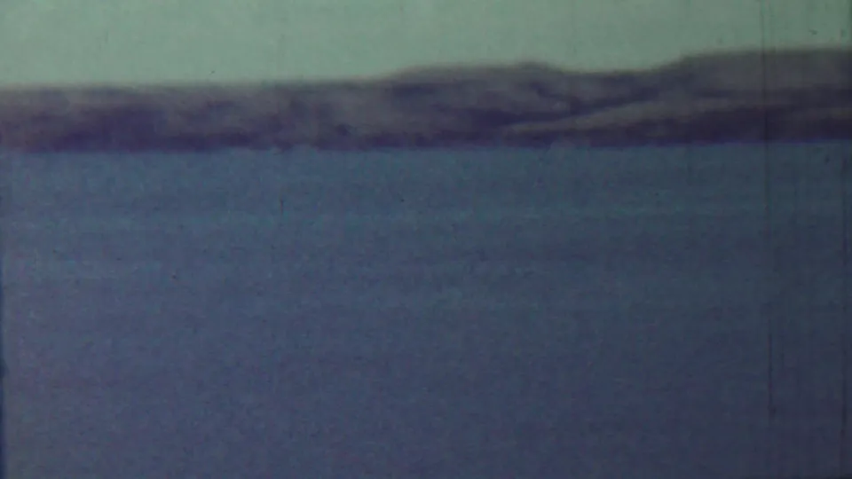 The pan continues across a broad water surface near Saint Francis, Kansas, with a low shoreline and visible 8mm film scratches.