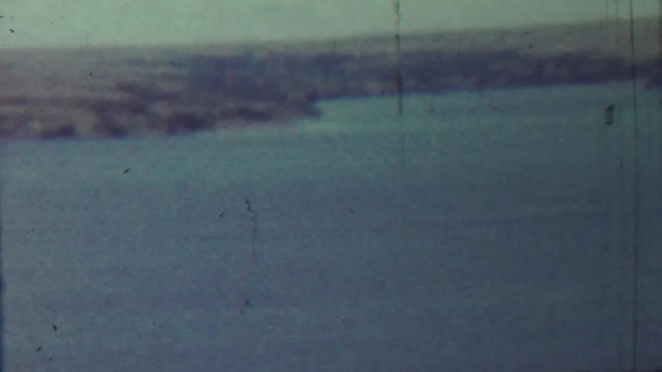 A mid-century 8mm frame of a quiet lake or reservoir, with the shoreline softened by haze and film wear.