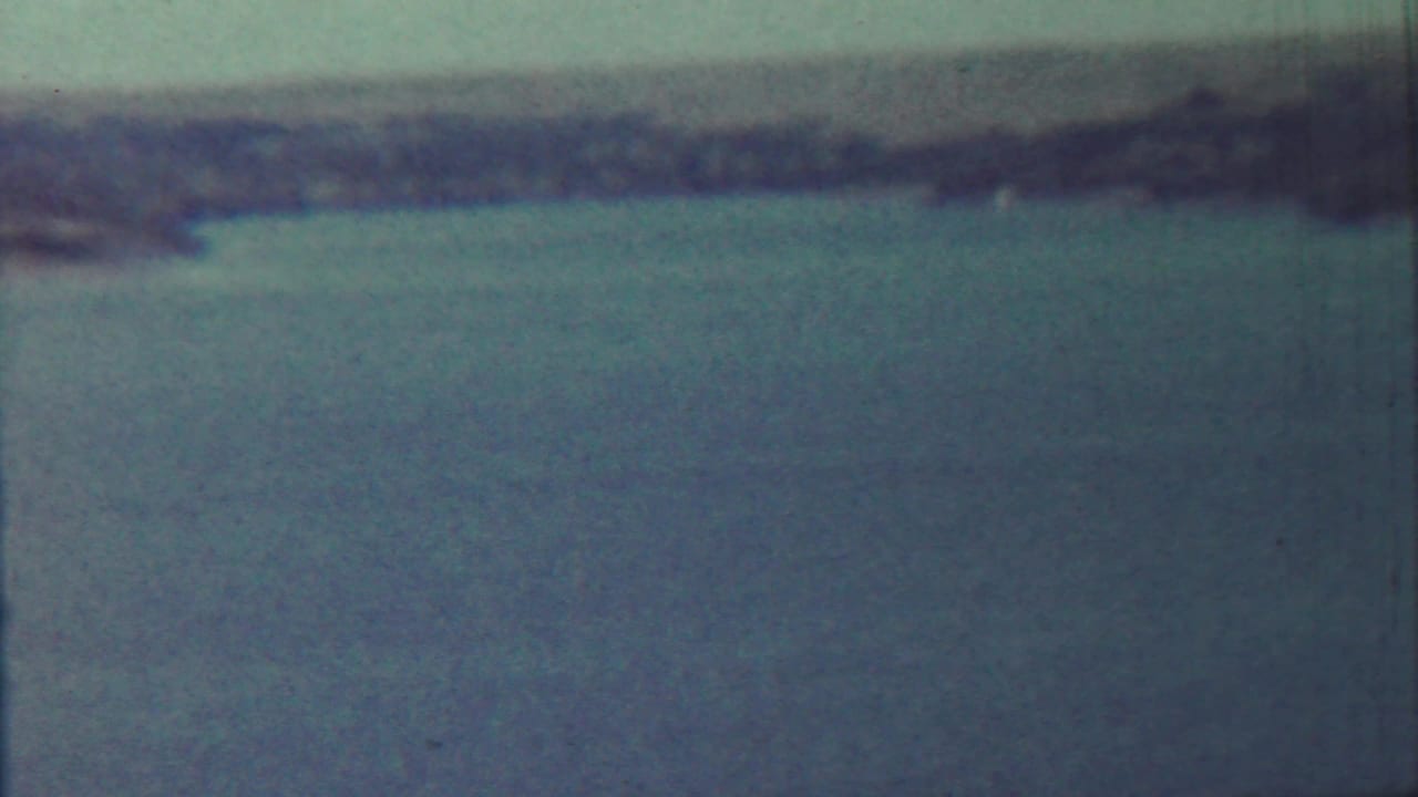 1959 8mm view near Saint Francis, Kansas, showing blue lake water, tall grass, and distant low hills with strong film wear visible.