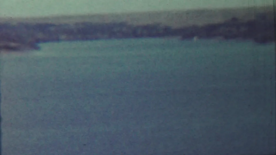 1959 8mm view near Saint Francis, Kansas, showing blue lake water, tall grass, and distant low hills with strong film wear visible.