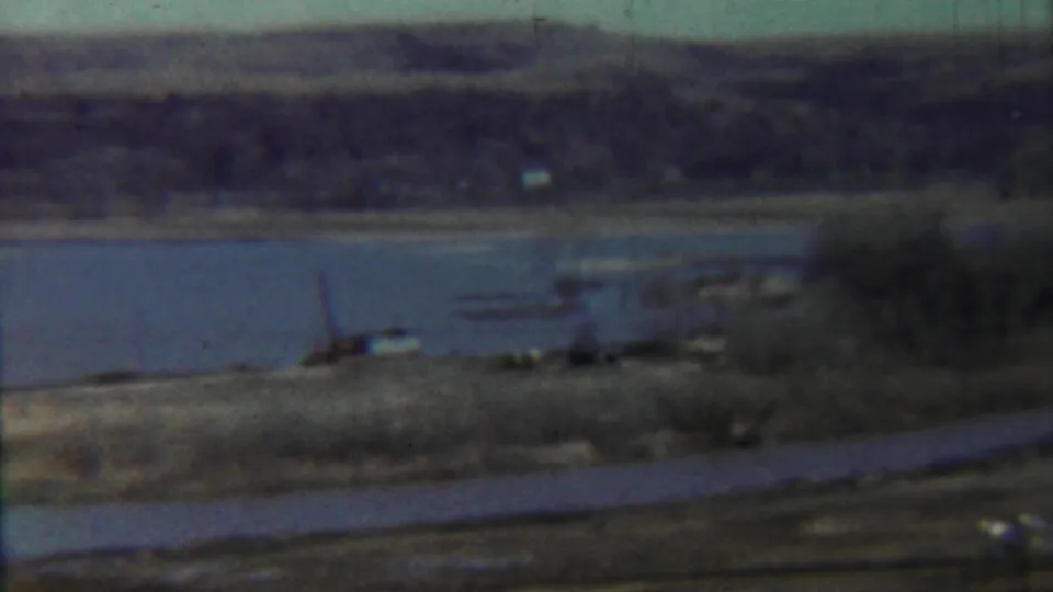 Saint Francis, Kansas lakeside view from 1959 with water, distant hills, dry grass, and a small structure or equipment near the shore.
