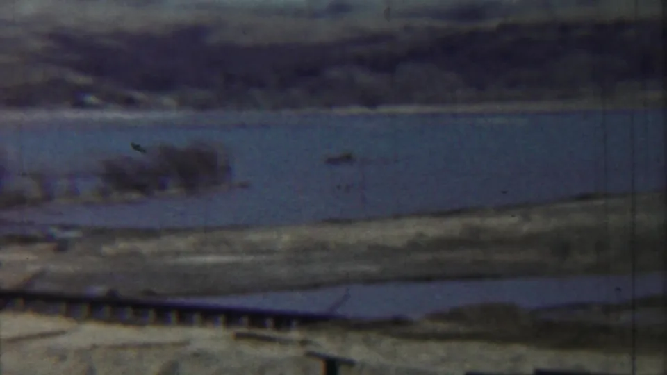 1959 Saint Francis, Kansas frame showing a quiet riverside scene with water, shoreline trees, and a low bridge or pier.