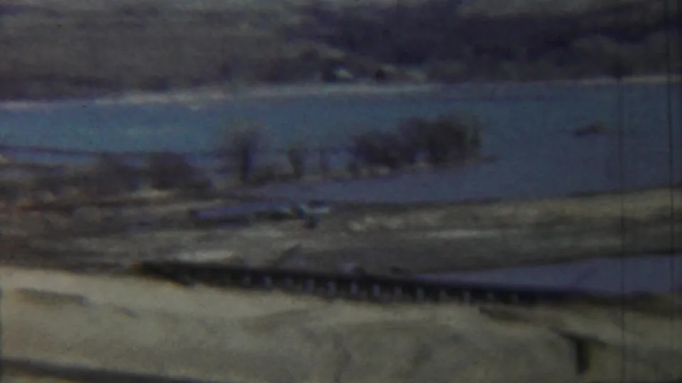 1959 Saint Francis, Kansas home-movie frame with a low bridge or pier, broad water, and a small boat near the right edge.