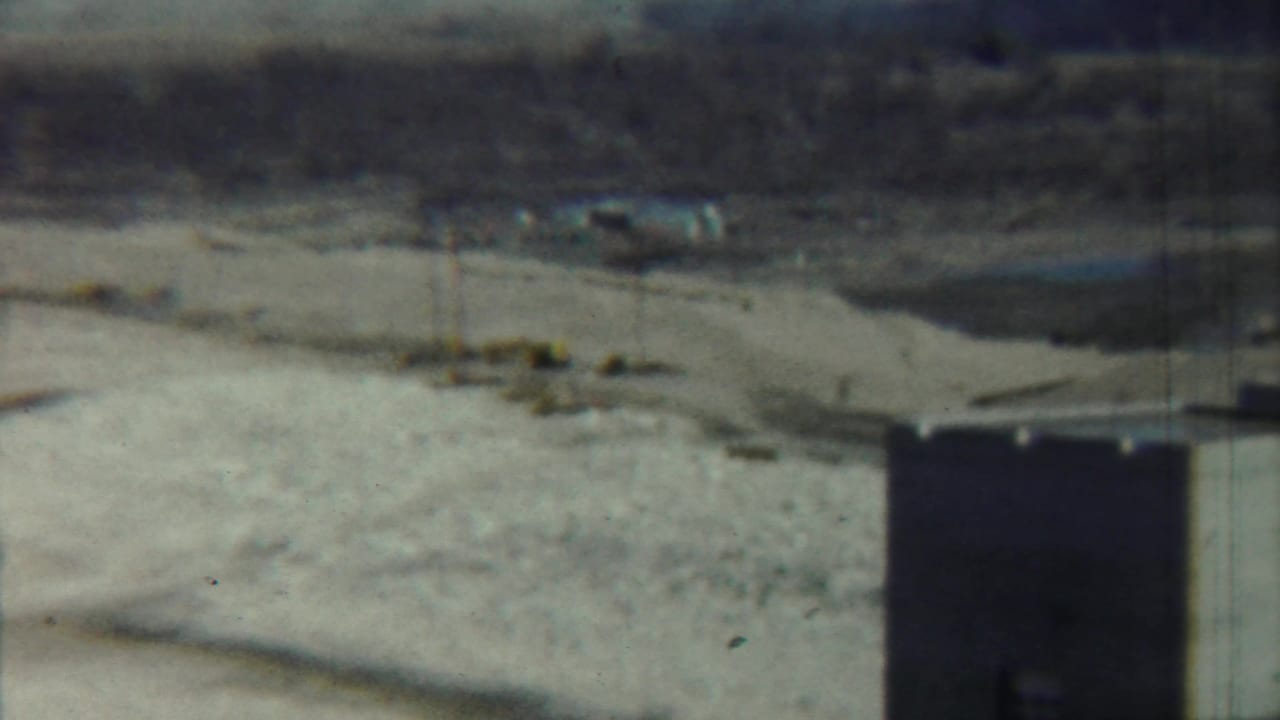 Concrete tower at right with pale field, utility poles, and small distant structures beyond.