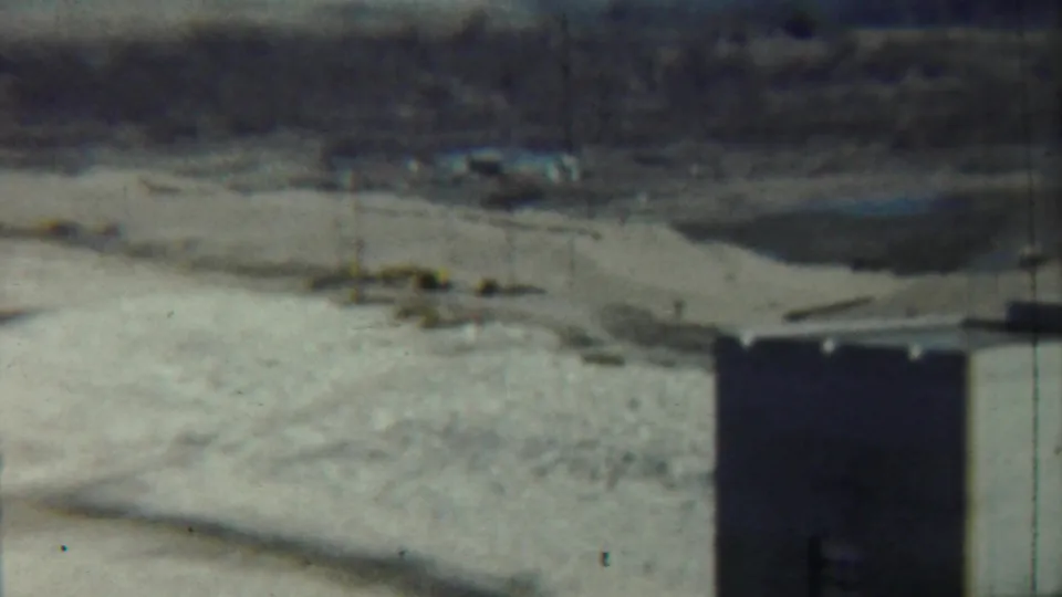 1959 Saint Francis, Kansas 8mm frame showing a tower corner in the foreground and a quiet rural field with poles and distant buildings.