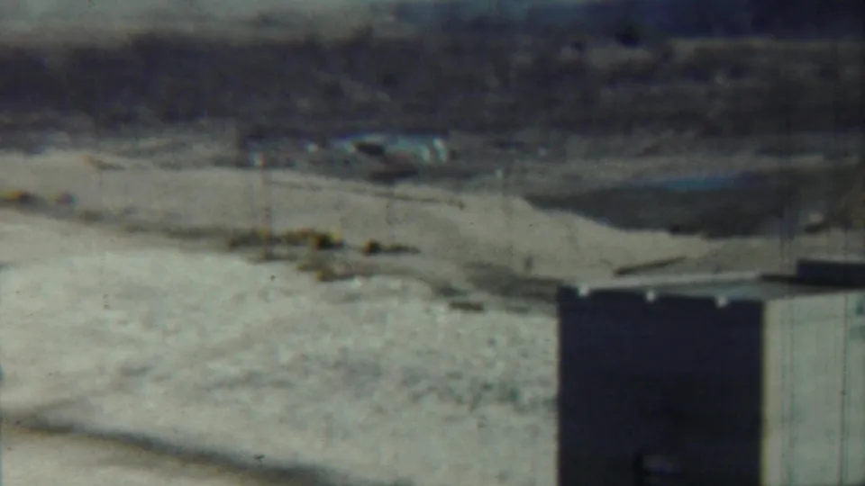 1959 Saint Francis, Kansas frame with a concrete tower at lower right, open sunlit field, utility poles, and distant low structures.