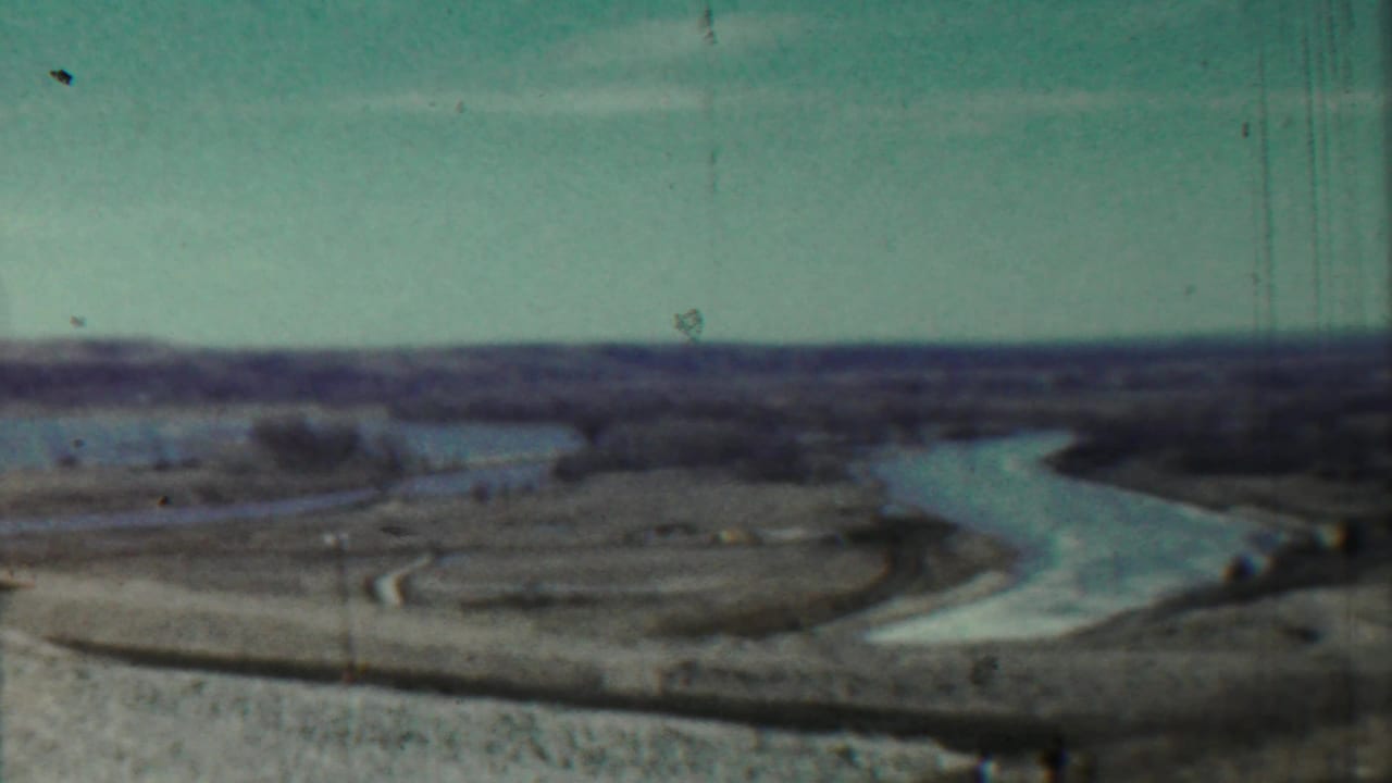 1959 8mm home-movie frame near Saint Francis, Kansas, showing a winding river through open countryside beneath a pale sky.